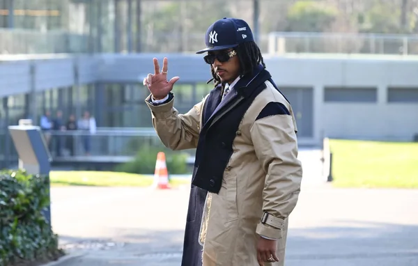Un joueur de l'équipe de France en trench coat beige et casquette bleue arrivant à Clairefontaine.