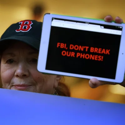 Un individu tenant une tablette avec le message 'FBI, DON'T BREAK OUR PHONES!' pour protester contre le déverrouillage d'iPhone.