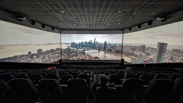 Un grand écran panoramique de cinéma avec un paysage urbain et des spectateurs.