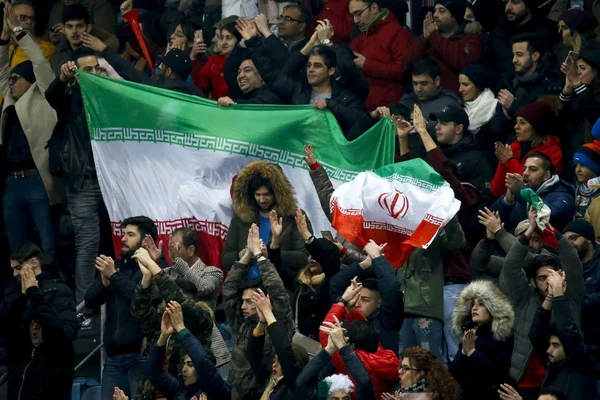Supporteurs iraniens brandissant des drapeaux nationaux et applaudissant lors d'un rassemblement sportif.