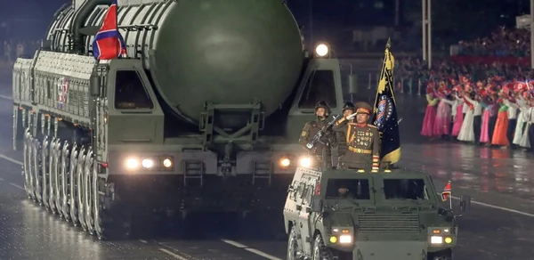 Un transporteur de missiles nord-coréen défile de nuit à Pyongyang sous les regards d'une foule en tenue traditionnelle.