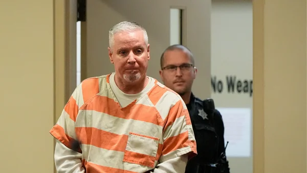 Colin Gray en tenue de prisonnier marchant dans un couloir avec un officier.