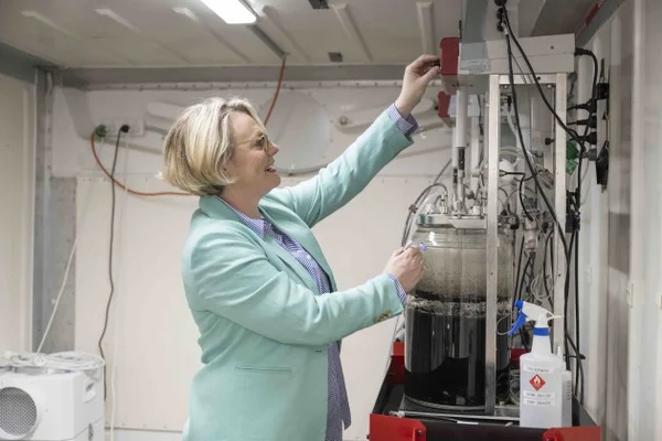 Une femme en blouse devant un équipement de laboratoire complexe avec un cylindre en verre.