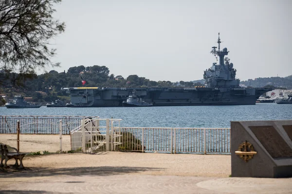 Le porte-avions Charles de Gaulle dans un port avec une promenade en bord de mer.