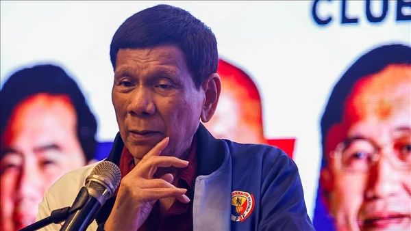 Personne en veste sombre s'adressant à la foule dans un cadre festive.