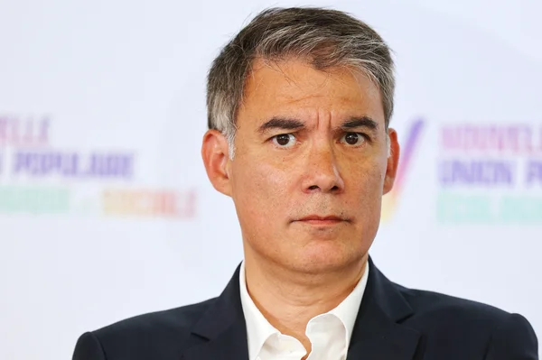 Cadrage serré sur le visage d'Olivier Faure en costume, sur un fond lumineux.