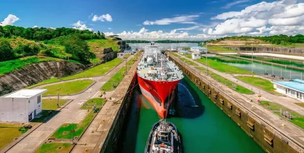Un navire cargo rouge navigue dans les écluses du canal de Panama, accompagné d'un remorqueur.