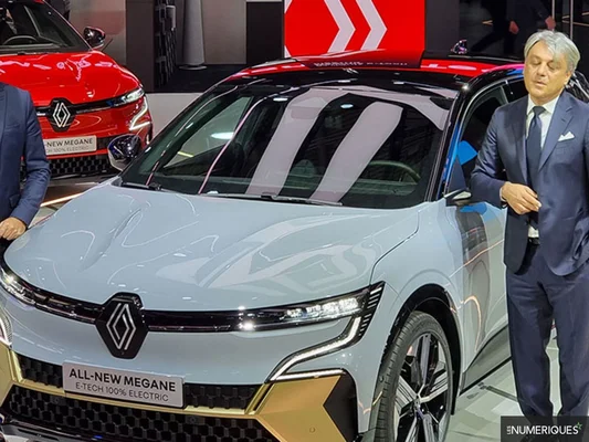 La Renault Megane E-Tech 100% électrique bleu clair présentée à un salon automobile avec une Megane rouge en arrière-plan.