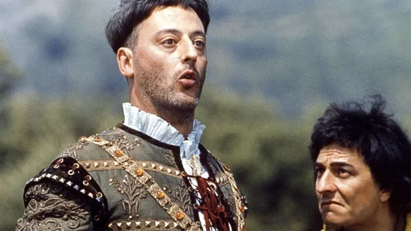 Acteurs en costumes médiévaux sur le plateau de Les Visiteurs, avec une tunique brodée et une coiffure volumineuse caractéristiques.