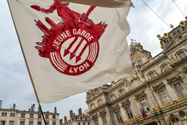 Drapeau Jeune Garde Lyon déployé devant un bâtiment orné d'une horloge.
