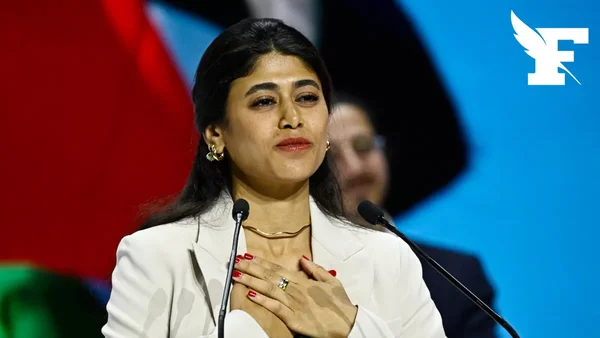 Rima Hassan se tient à un podium avec des micros lors d'une déclaration publique.