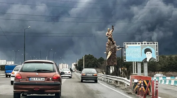 Une route avec des voitures roulant sous un ciel orageux sombre, devant une statue et un panneau d'affichage.