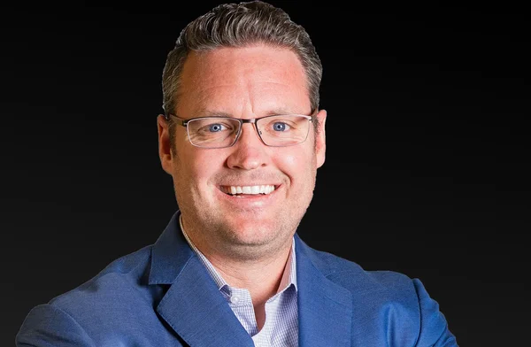 Portrait de Trevor Milton souriant en blazer bleu.