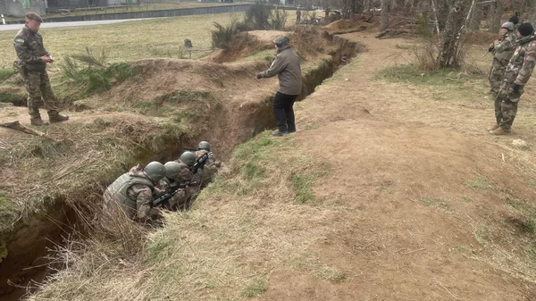 Soldats en camouflage dans une zone boisée, l'un manipulant des munitions.