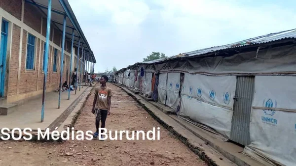 Allée du camp entre un bâtiment et des tentes du HCR, symbolisant l'attente des réfugiés.