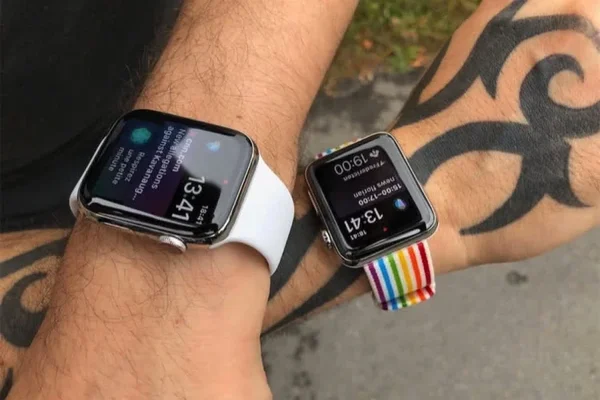 Deux Apple Watch aux poignets, avec bracelets blanc et arc-en-ciel, à côté d'un tatouage tribal