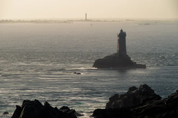 Le phare de la Vieille devant l'île de Sein sous la lumière du soir, avec au loin les phares d'Ar Men et le Grand phare de l'île de Sein.