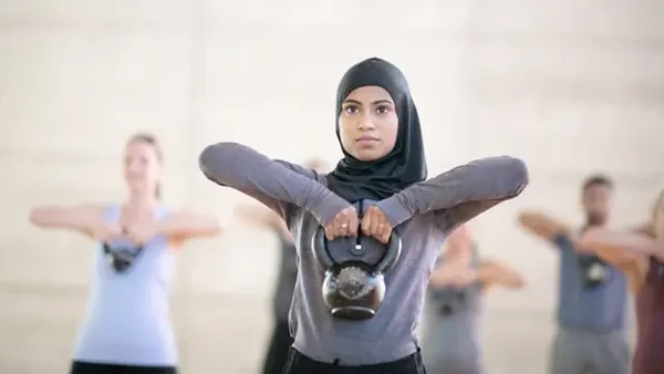 Une femme voilée tient un kettlebell devant elle lors d'un entraînement de groupe.