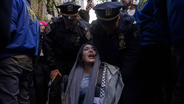 Deux policiers encadrant une femme en détresse lors d'un rassemblement public.