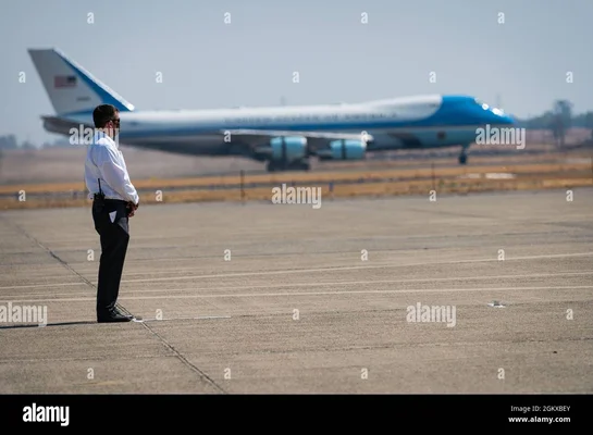 Un agent du Secret Service sur le tarmac face à un avion présidentiel bleu et blanc.