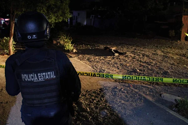 Policier en uniforme de la Policía Estatal debout près d'un ruban de signalisation jaune la nuit.