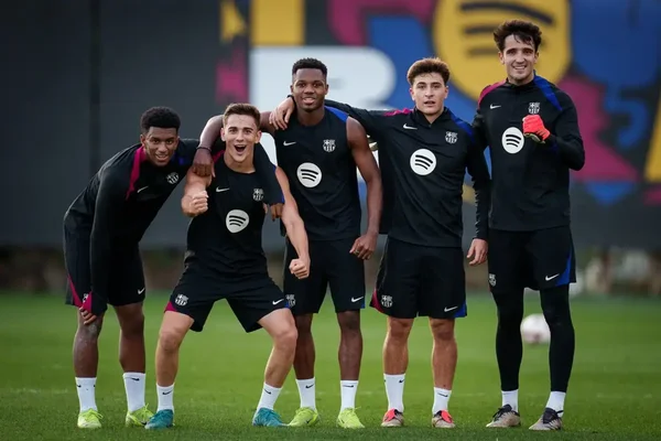 Groupe de joueurs du Barça posant en tenue noire d'entraînement sur le gazon de la Ciutat Esportiva.