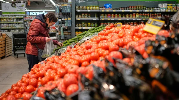 Une personne sélectionnant des tomates et des concombres au supermarché.