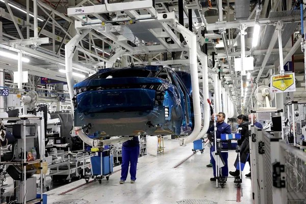 Carrosserie automobile bleue sur la ligne d'assemblage avec des ouvriers en uniforme bleu à l'ouvrage.