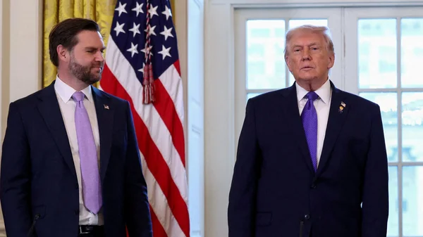 Deux hommes en costume debout devant un drapeau américain.