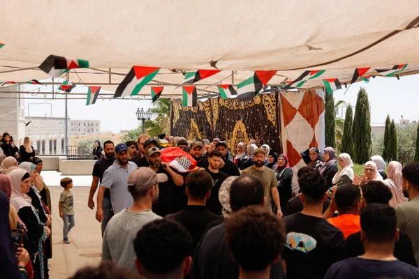 Une procession funèbre a lieu sous une tente décorée de drapeaux palestiniens, avec des porteurs et des endeuillés