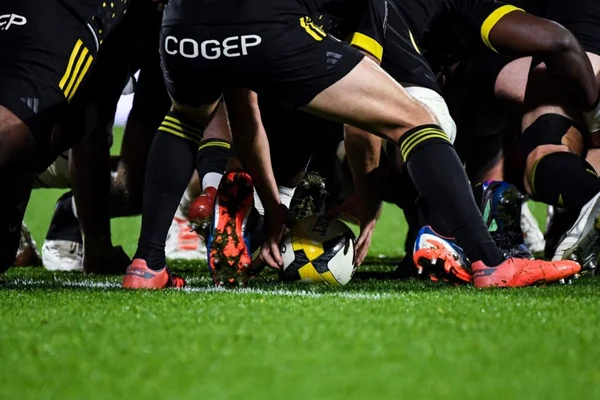 Action de jeu entre des rugbymen portant des maillots noirs aux accents jaunes.