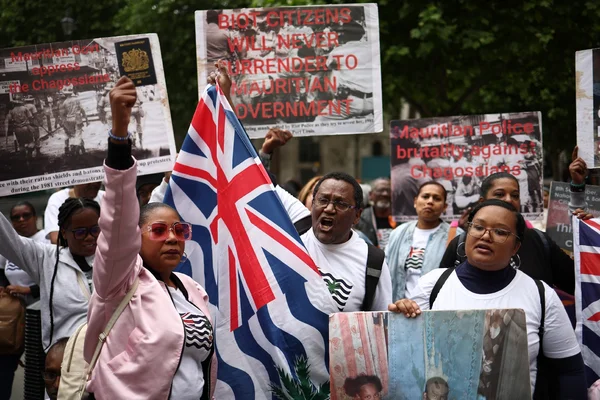 Manifestation avec panneaux critiquant le gouvernement mauricien et drapeau britannique.