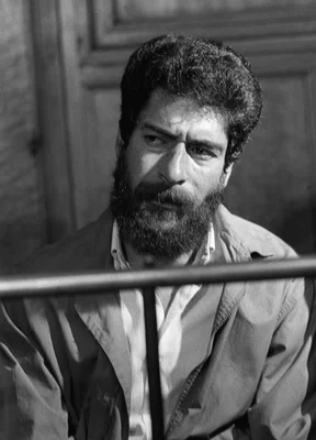 Georges Ibrahim Abdallah assis, portrait en noir et blanc avec barre horizontale au premier plan.