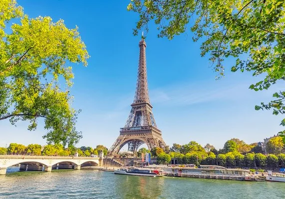 La tour Eiffel dominating le ciel bleu au-dessus de la Seine et de ses berges arborées.