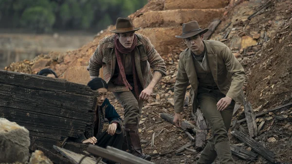 Trois personnages en costume du début du XXe siècle dans un lieu encombré.