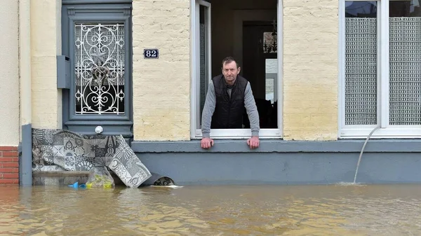 Un homme regarde l'eau atteindre la base de son immeuble depuis une fenêtre.