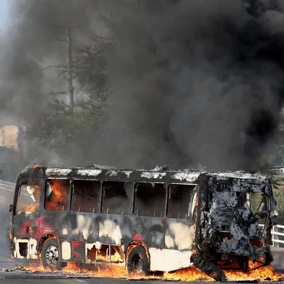 Un bus entièrement en flammes avec une épaisse fumée noire montant dans le ciel.