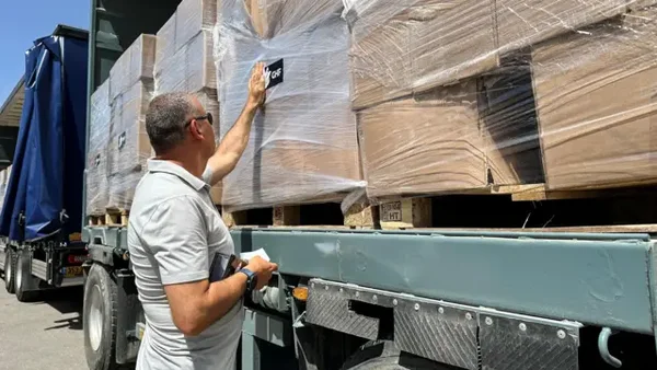 Un homme touche des palettes chargées sur un camion avec une bâche bleue.