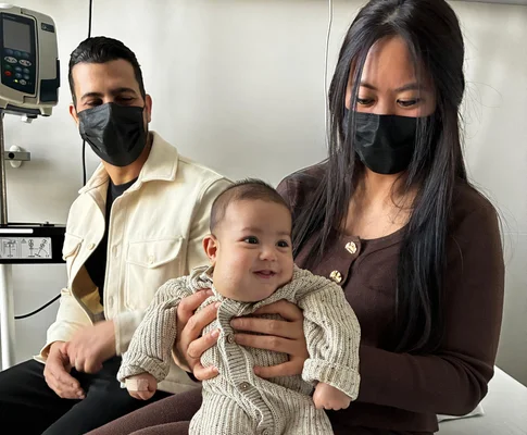 Les parents portant des masques tiennent leur bébé souriant dans un cadre médical.