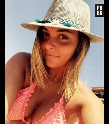 Priscilla Betti portant un chapeau de paille décoré et un haut de maillot rayé.