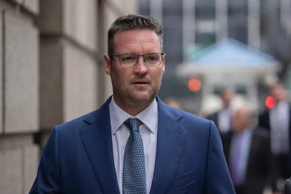 Trevor Milton standing dans un environnement urbain avec des bâtiments en arrière-plan.