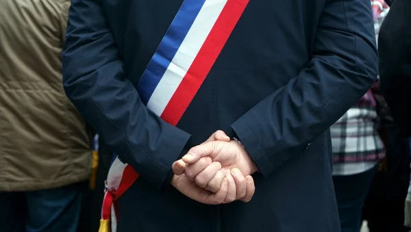 Une personnalité en écharpe tricolore de dos, entourée d'autres personnes lors d'un événement.