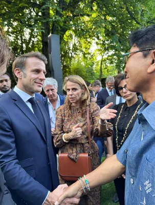 Emmanuel Macron et Lee Soo-man lors d'une poignée de main en extérieur, entourés de proches collaborateurs.