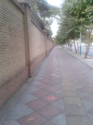 Un trottoir carrelé longeant un mur de briques avec des arbres, aux abords de l'ambassade britannique.