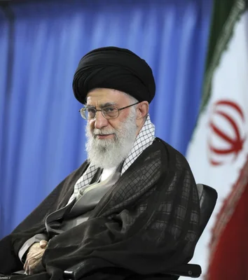 L'Ayatollah Ali Khamenei assis devant un rideau bleu et un drapeau iranien.