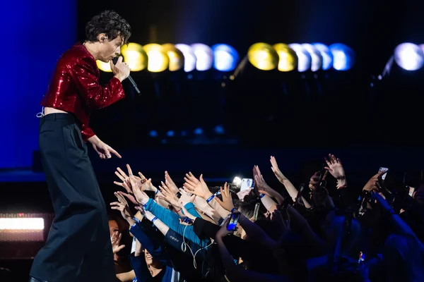 Harry Styles chantant et tendant la main au public