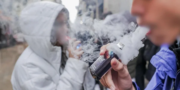 Deux personnes à l'extérieur, l'une tenant une cigarette électronique qui émet de la fumée.