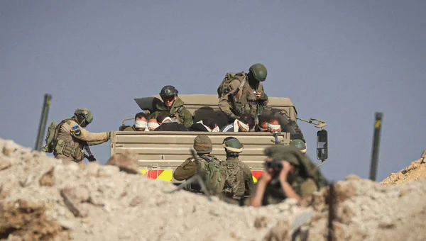 Des soldats armés entourant un camion transportant des détenus aux yeux bandés