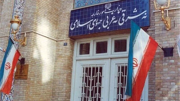 Entrée d'un bâtiment officiel avec deux drapeaux iraniens et une inscription en persan.