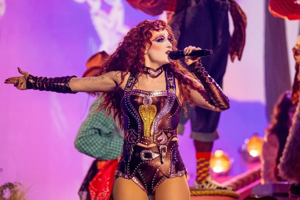 Chappell Roan sur scène, vêtue d'un costume métallique violet et or scintillant.